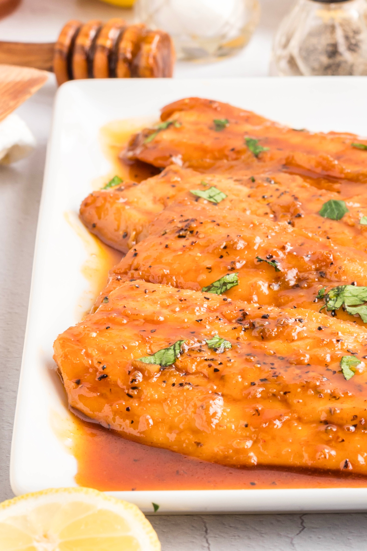 Honey glazed salmon fillets coated in a glossy honey glaze with butter, soy sauce, and lemon, finished with black pepper and parsley on a white platter.