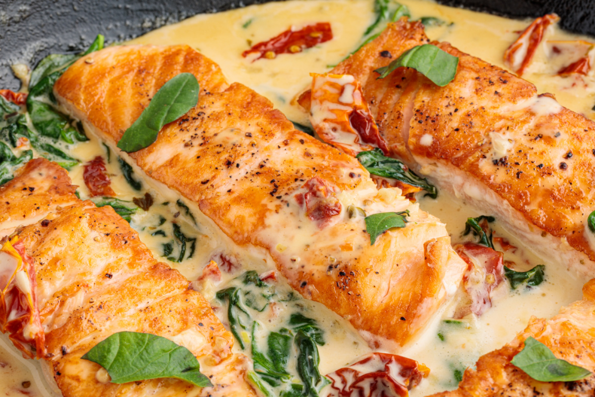 One pan Tuscan salmon cooking in a skillet with a creamy garlic sauce, sun-dried tomatoes, and wilted spinach.