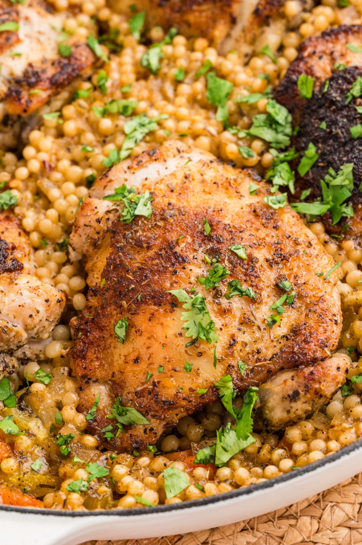 Crispy chicken thighs over pearl couscous baked in a wide pan with lemon, herbs, and vegetables.
