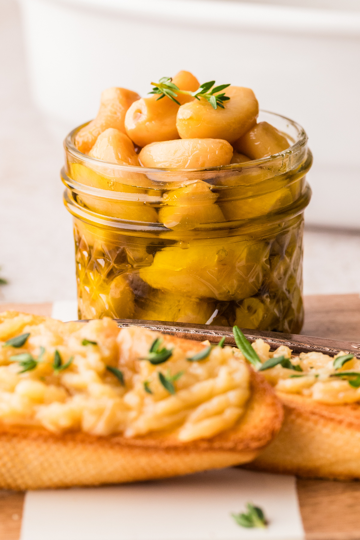 Step-by-step process showing garlic cloves submerged in olive oil before and after slow cooking in the oven.