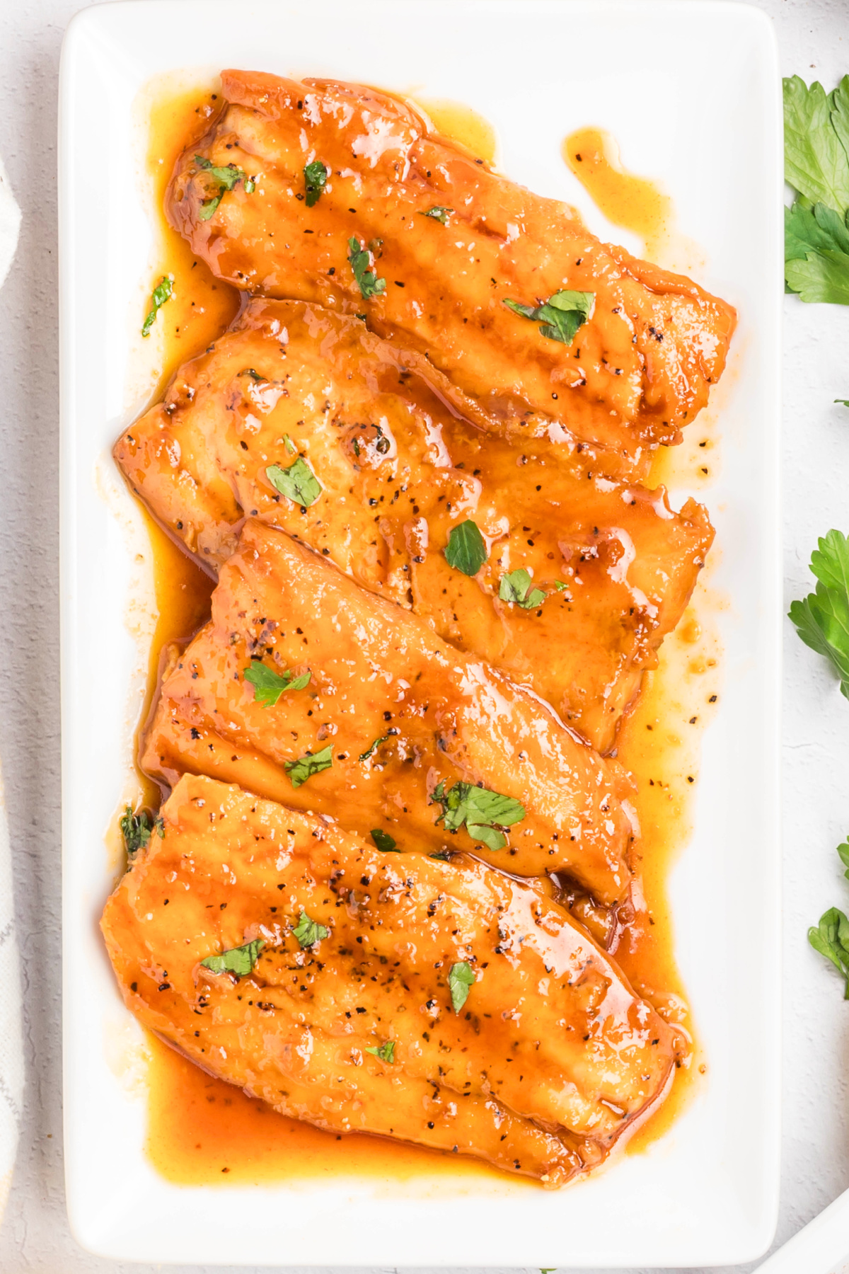 Honey glazed salmon fillets arranged on a platter, fully coated in a smooth honey glaze and finished with black pepper and parsley.