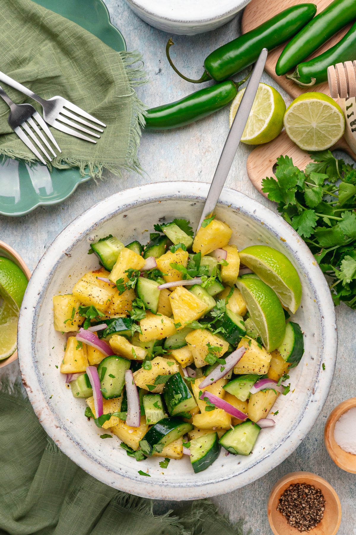 Chilled pineapple cucumber salad with fresh pineapple, cucumber, red onion, serrano pepper, cilantro, and lime wedges in a bowl.