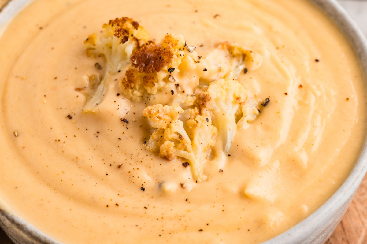 Creamy cauliflower soup with roasted cauliflower florets and cracked black pepper blended smooth in a shallow bowl.
