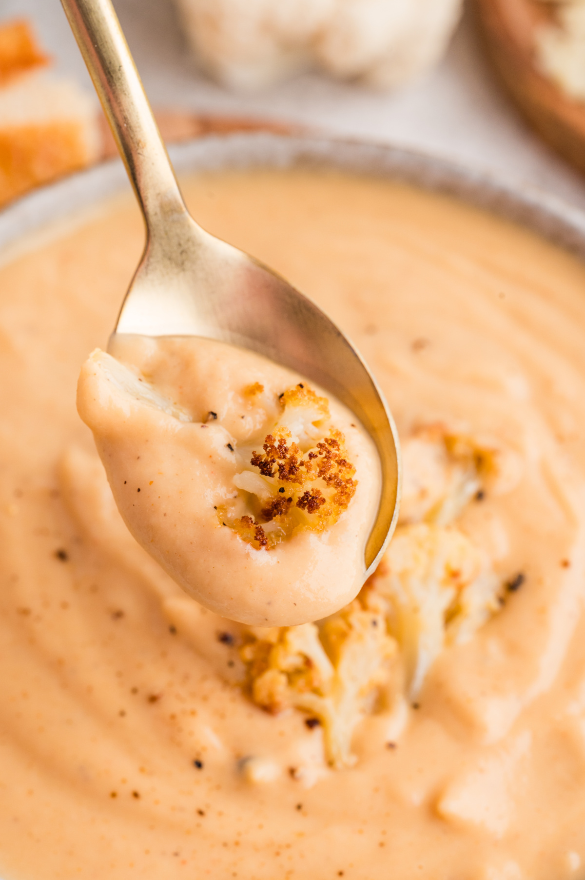 A spoonful of creamy cauliflower soup with a piece of roasted cauliflower lifted from the bowl.