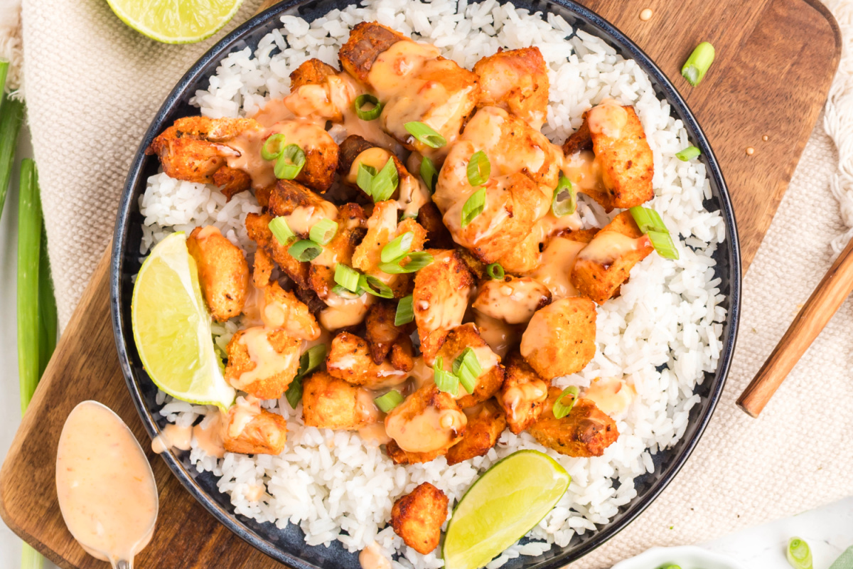 Air fryer bang bang salmon bites served over white rice with creamy sauce, sliced green onions, and lime wedges.