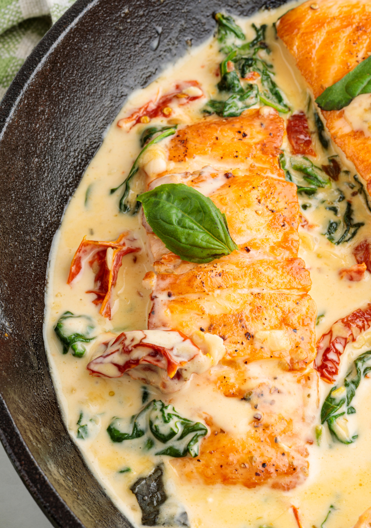 Marry Me Tuscan salmon simmering in a creamy garlic sauce with sun-dried tomatoes and wilted spinach in a cast iron skillet.