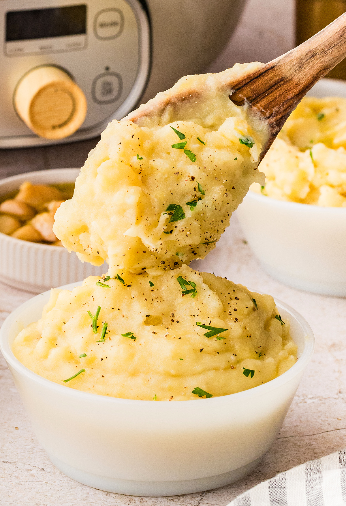 Creamy mashed potatoes being scooped with a wooden spoon, showing a soft texture and light seasoning while held warm.