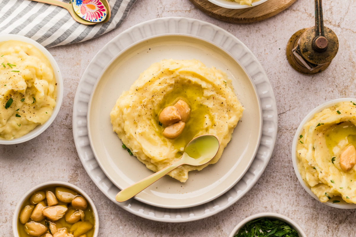 Slow cooker garlic confit mashed potatoes served on a plate with confit garlic cloves and garlic oil, showing a creamy texture ready for the table.