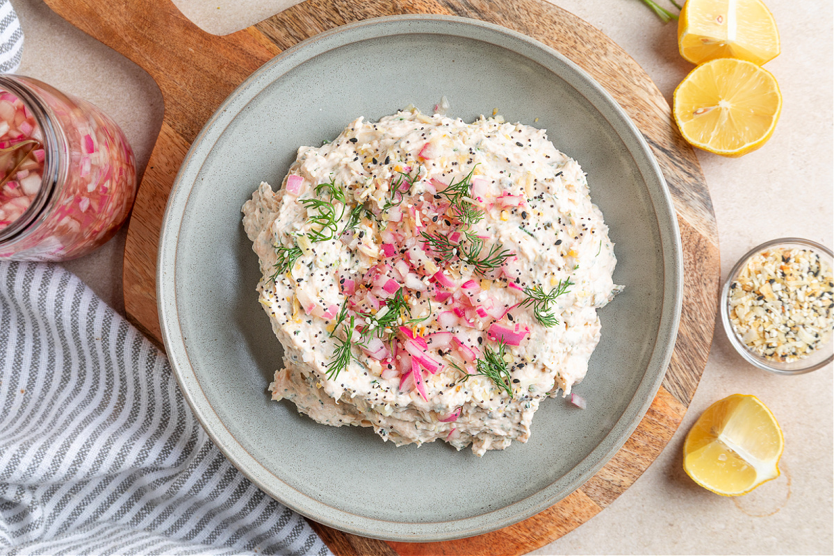 Smoked salmon dip with cream cheese, dill, capers, and pickled red onions, shown close up with a spoon ready to scoop.