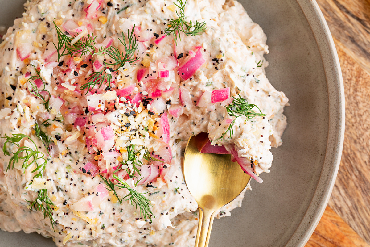 Creamy salmon dip topped with pickled red onions, fresh dill, and everything bagel seasoning, styled on a serving board with lemon halves.