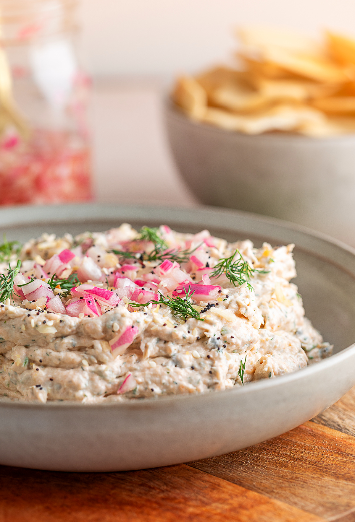 Smoked salmon dip topped with quick-pickled red onions, fresh dill, and everything bagel seasoning in a shallow serving bowl.