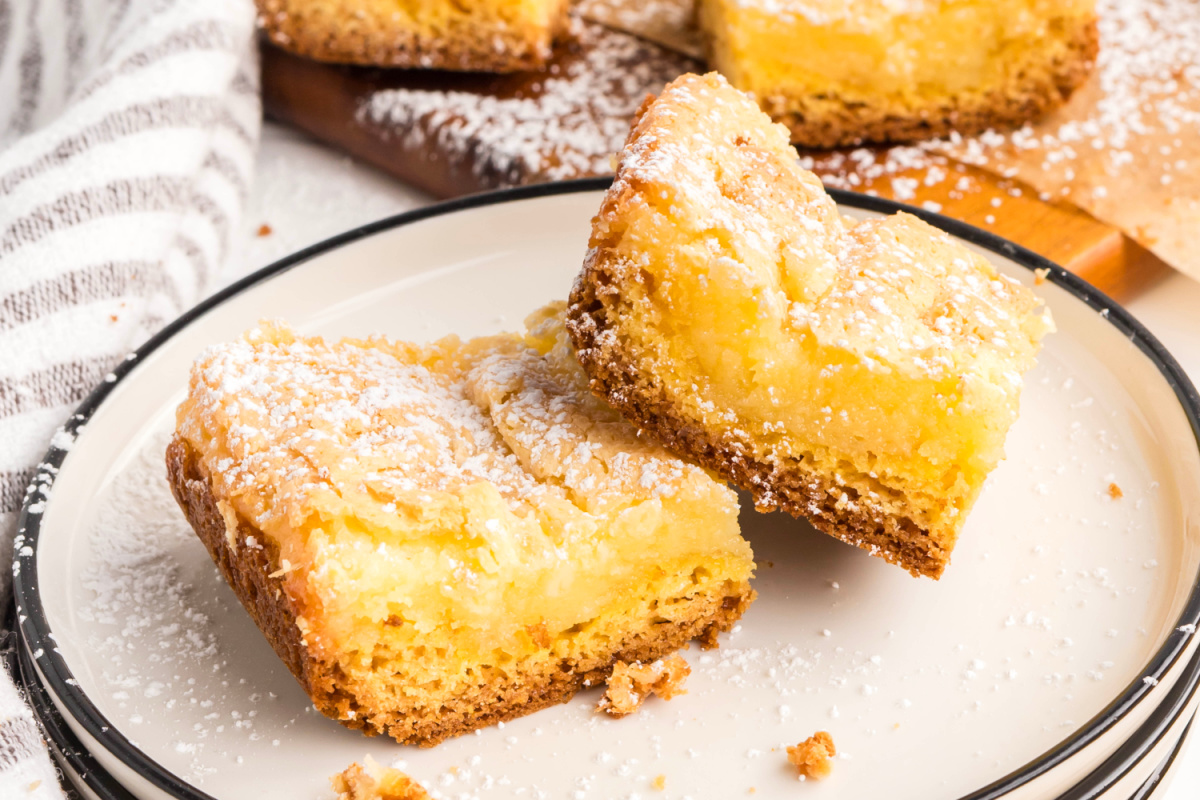Gooey butter cake bars with a rich cream cheese topping and buttery base, baked until golden and dusted lightly with confectioners&rsquo; sugar.