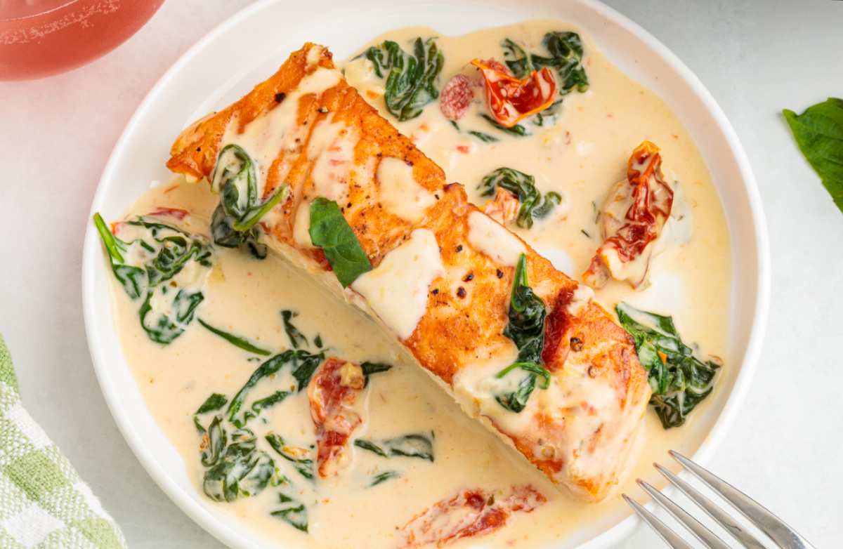 Creamy Tuscan salmon served in a shallow bowl with garlic cream sauce, sun-dried tomatoes, and wilted spinach.