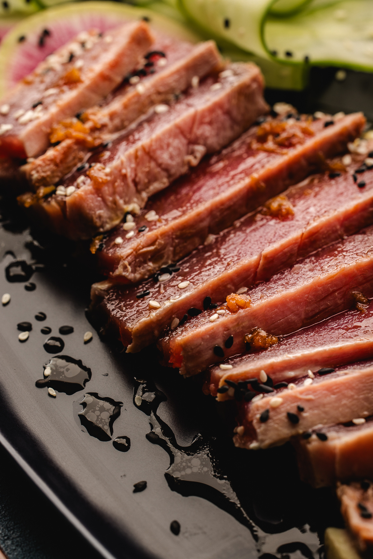 Rare ahi tuna slices with sesame seeds and ginger soy drizzle on a black plate
