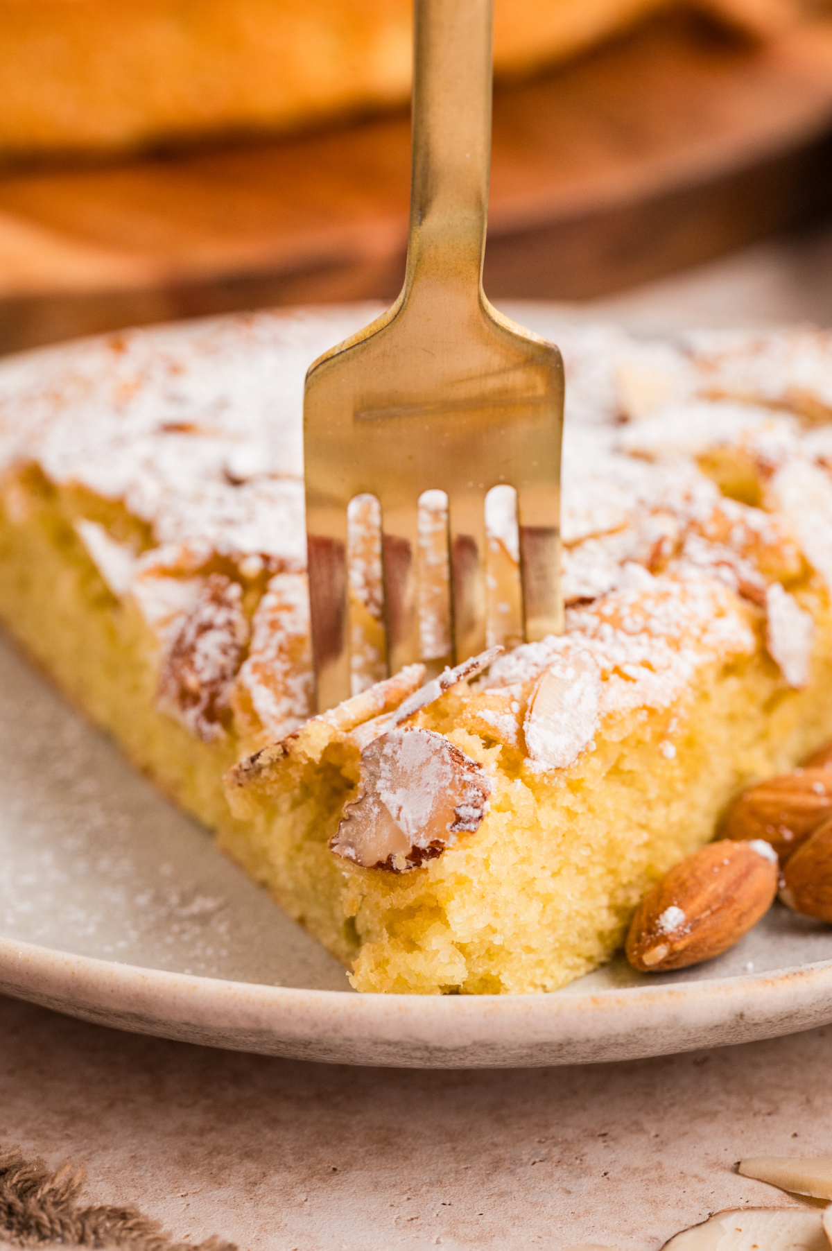 Close-up of almond flour cake slice with fork pressing into the soft crumb and sliced almonds on top