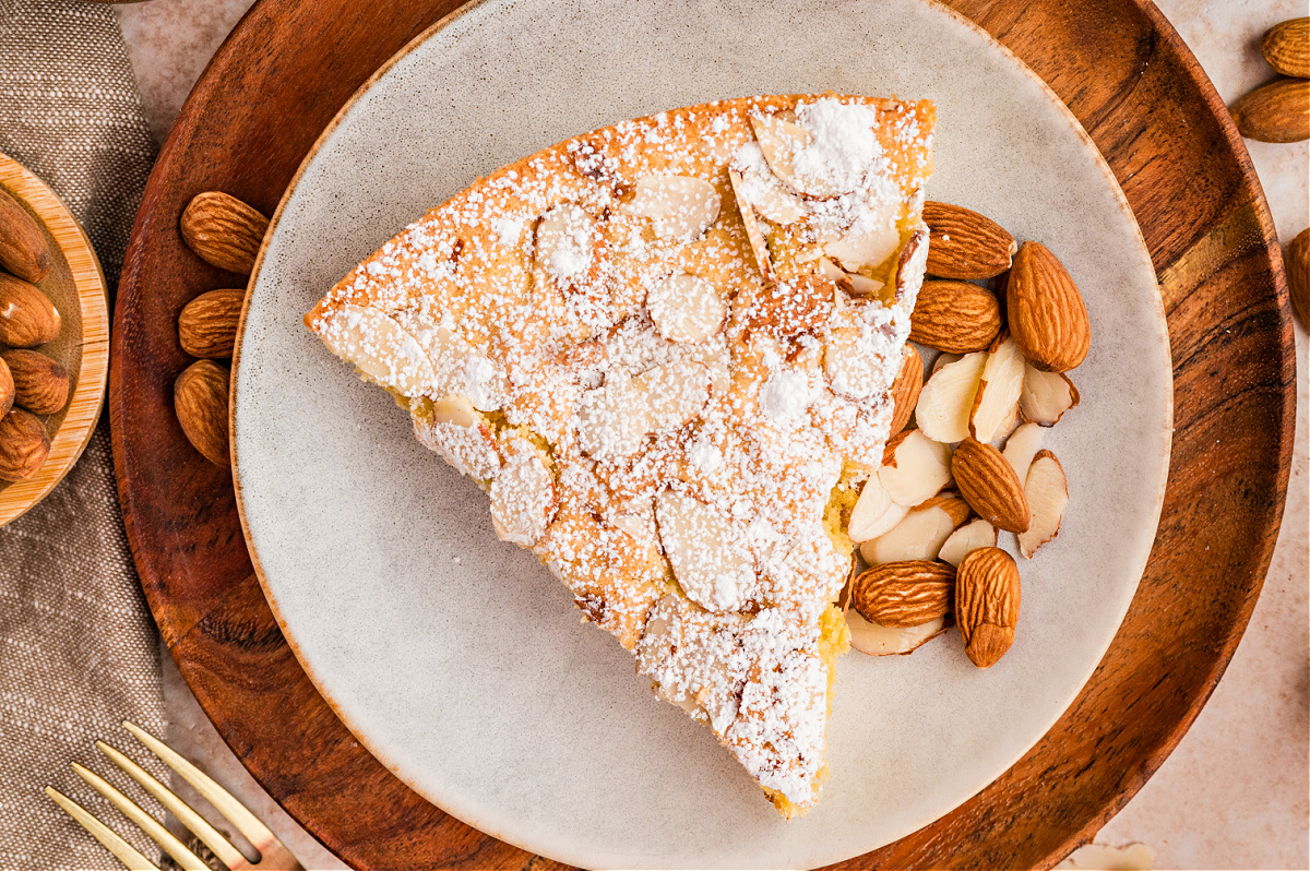 Overhead view of almond cake slice dusted with powdered sugar and topped with sliced almonds on a plate