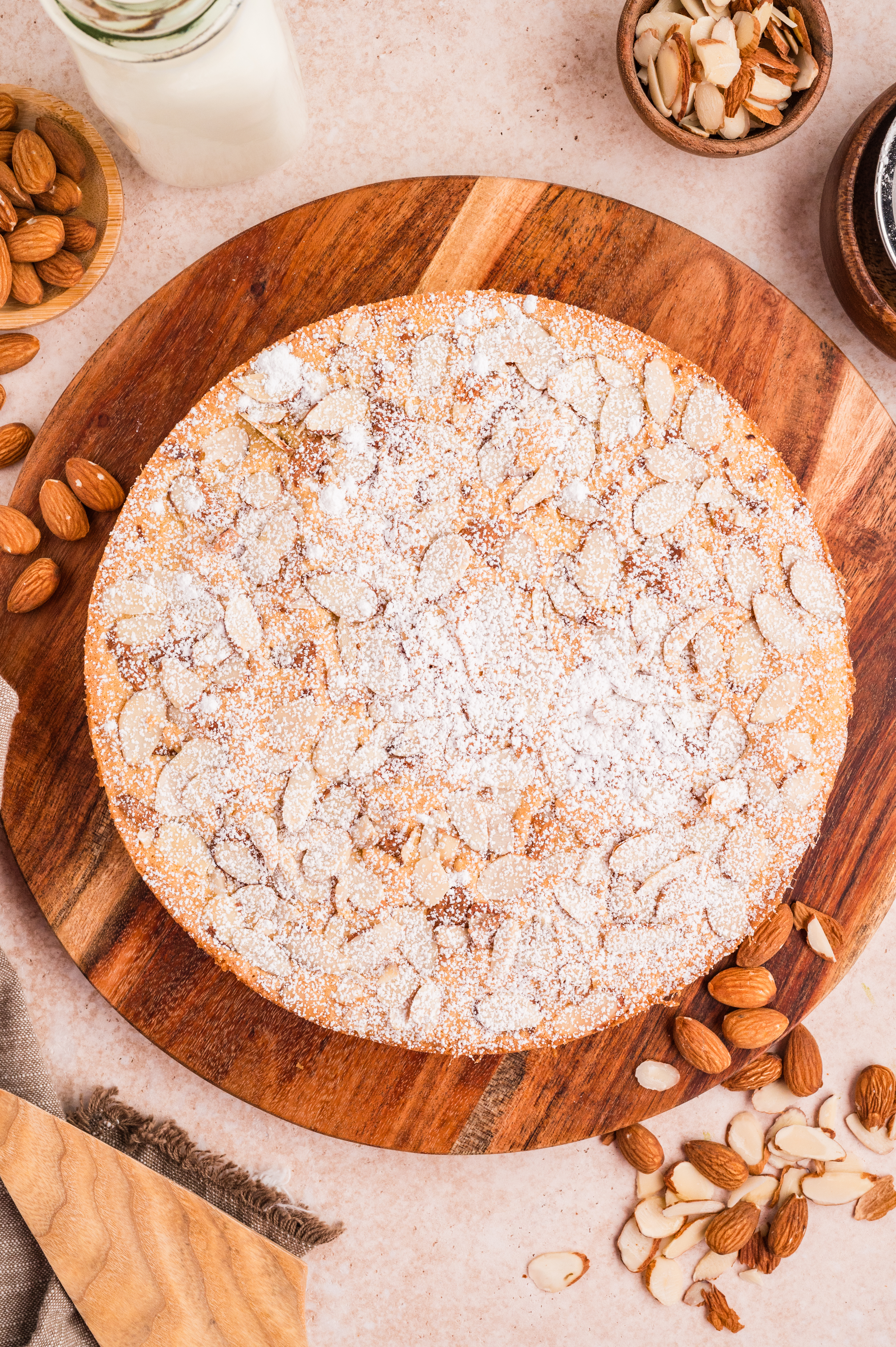Whole almond flour cake topped with sliced almonds and a dusting of powdered sugar on a wooden board