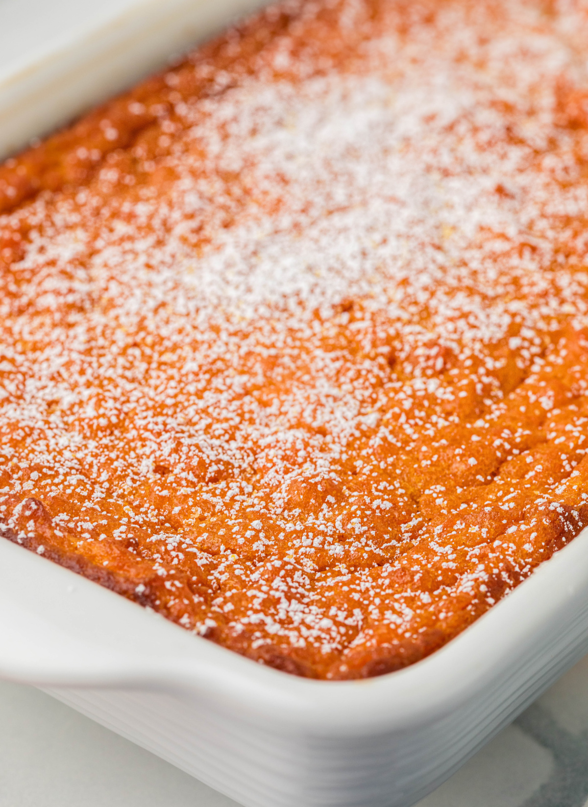 Powdered sugar being dusted over freshly baked Carrot Souffle in an 11x7 baking dish