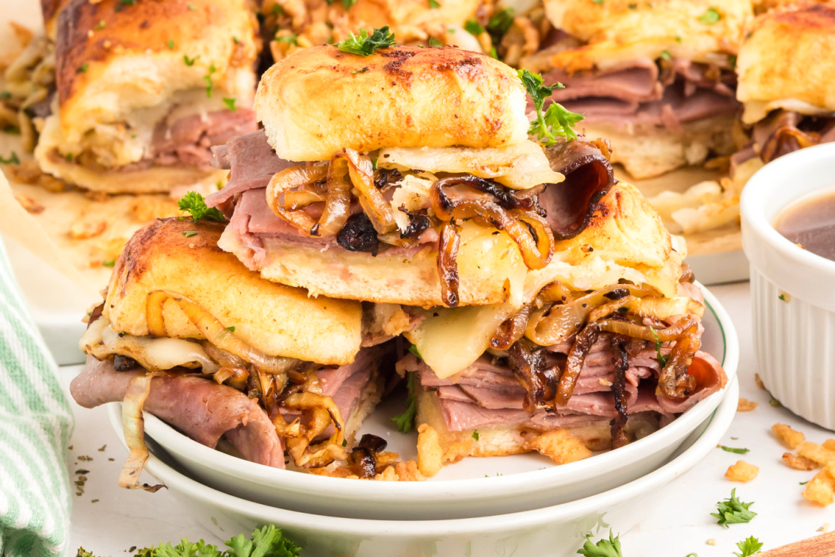 French dip sliders stacked with roast beef, melted provolone, caramelized onions, and au jus