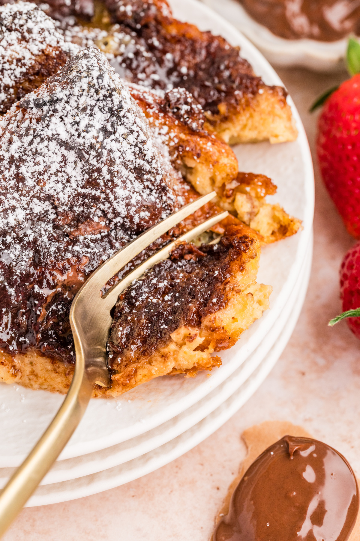 Close-up of chocolate hazelnut French toast casserole slice with powdered sugar and strawberries on a white plate