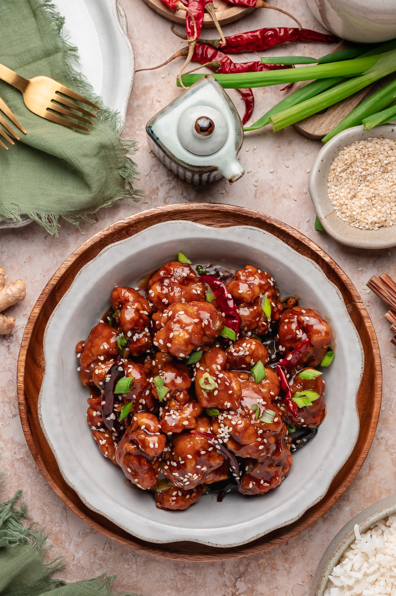 Bowl of crispy sweet and savory chicken topped with sesame seeds, scallions, and dried red chilies