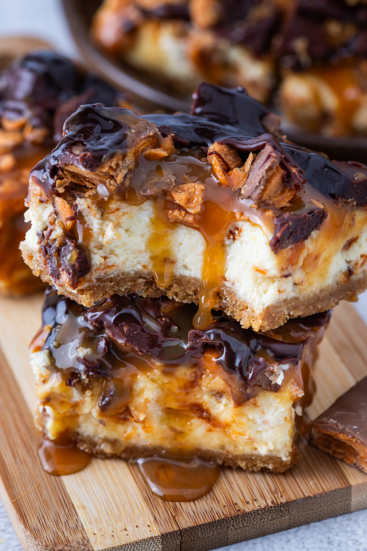Butterfinger Caramel Cheesecake Bars stacked with caramel drizzle and chopped Butterfingers over creamy cheesecake filling