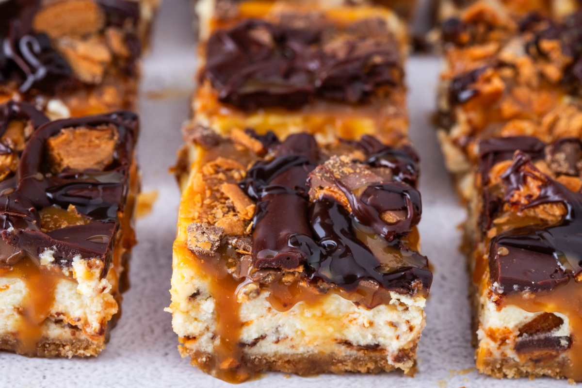 Butterfinger Caramel Cheesecake Bars sliced into squares with caramel drizzle and chocolate topping