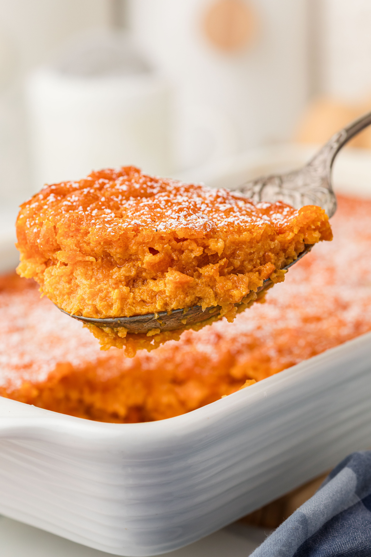 Spoon lifting a serving of Carrot Souffle from white baking dish