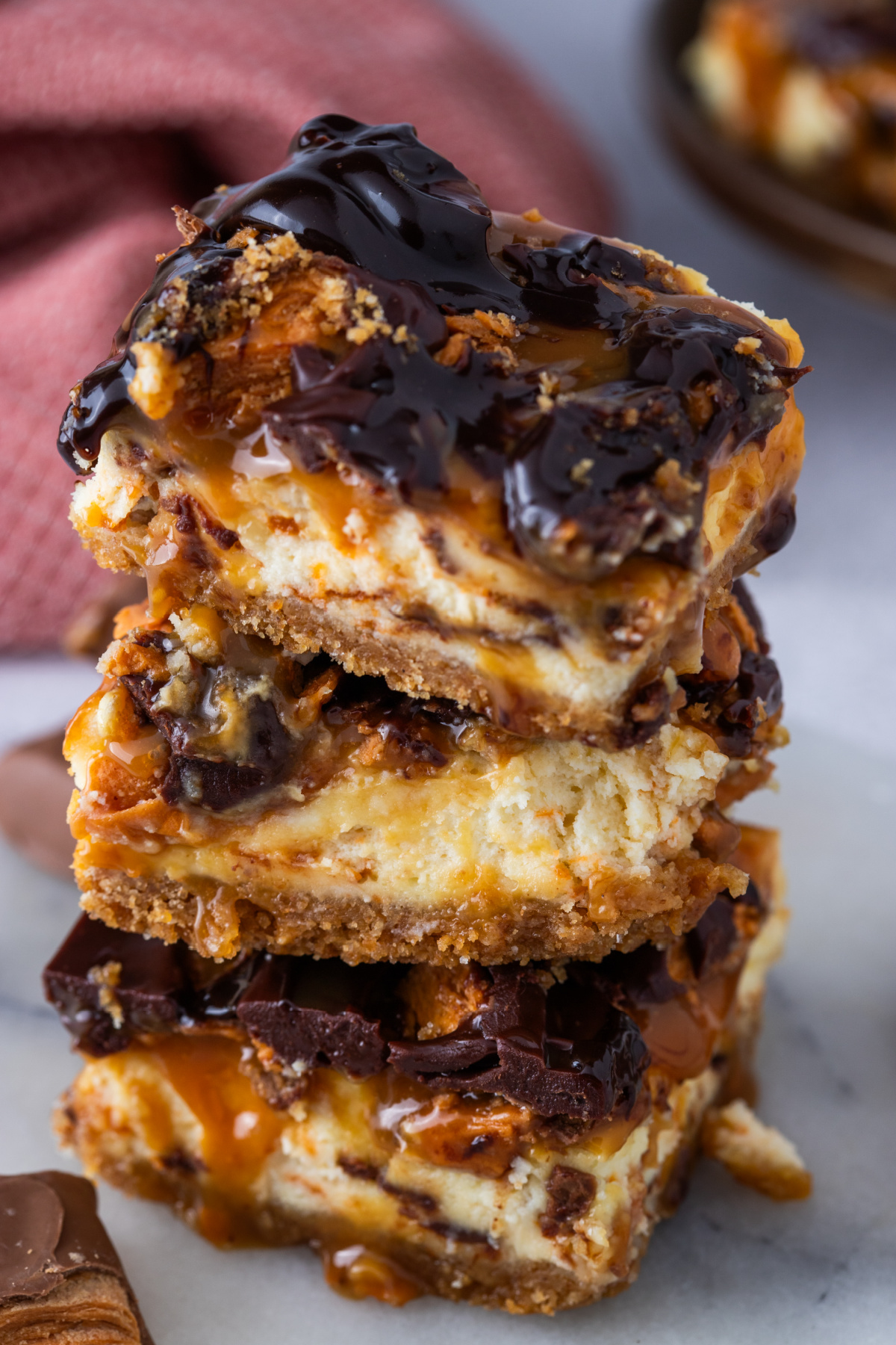 Stacked caramel cheesecake bars with chopped Butterfinger pieces and chocolate drizzle