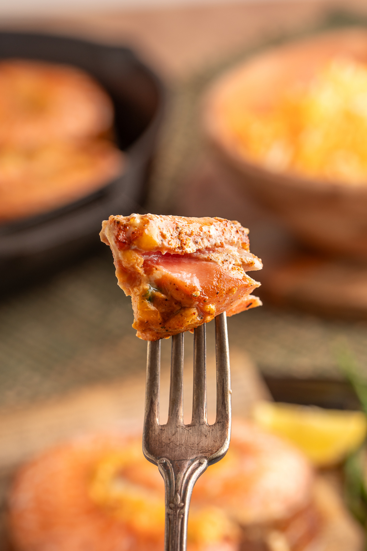 Close-up of a fork lifting a bite of baked stuffed salmon, showing tender layers of salmon and creamy jalape&ntilde;o popper-style filling.