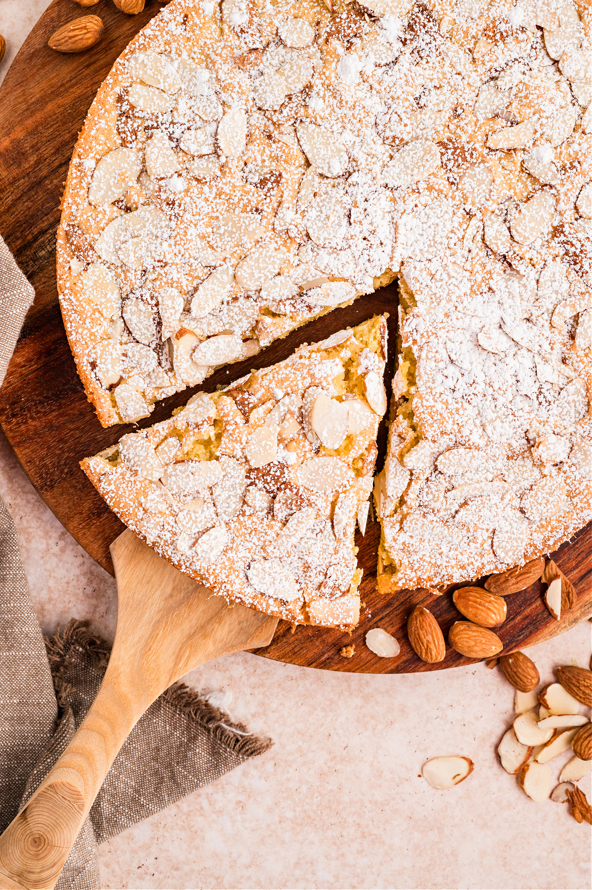 Overhead view of sliced almond flour cake with powdered sugar and toasted sliced almonds
