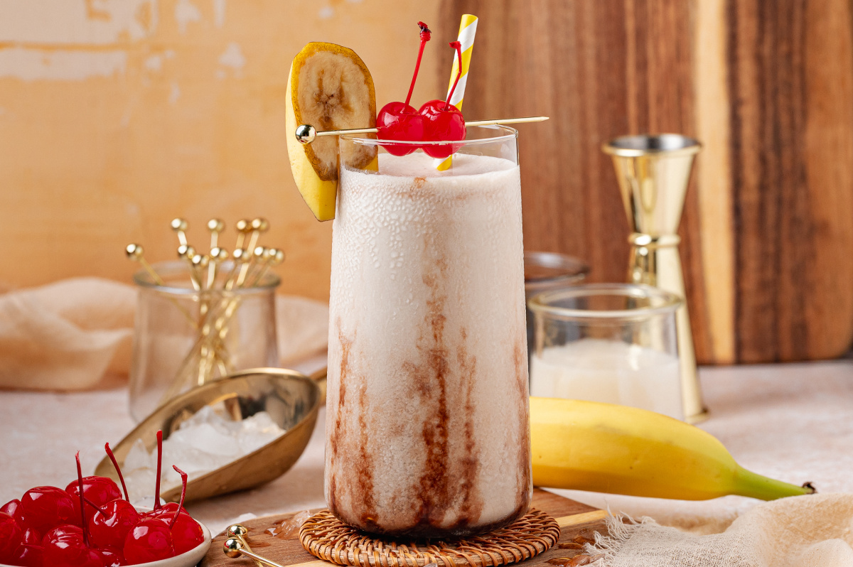 Creamy frozen banana cocktail with chocolate syrup swirls, cherries, and banana garnish