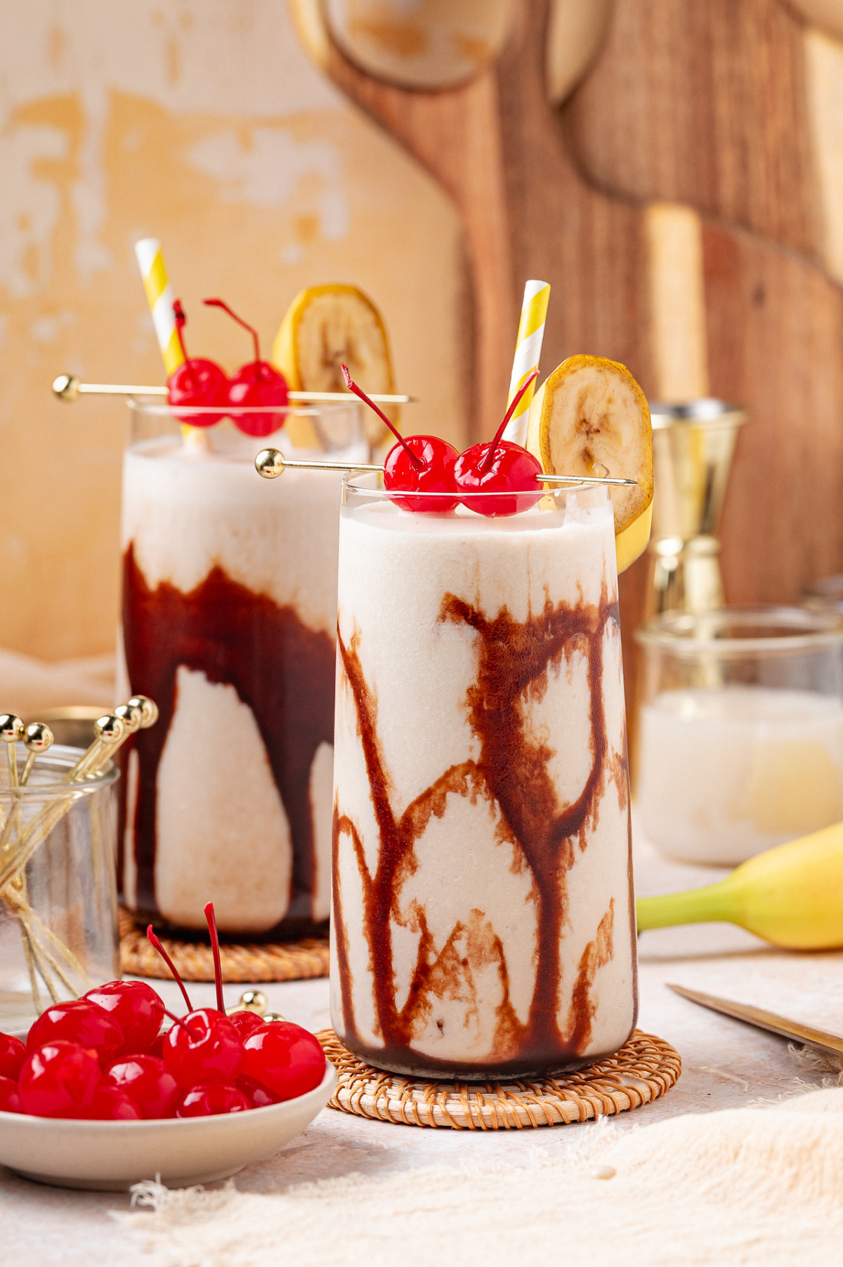Dirty Banana cocktail with chocolate syrup swirled inside the glass, topped with maraschino cherries and banana garnish