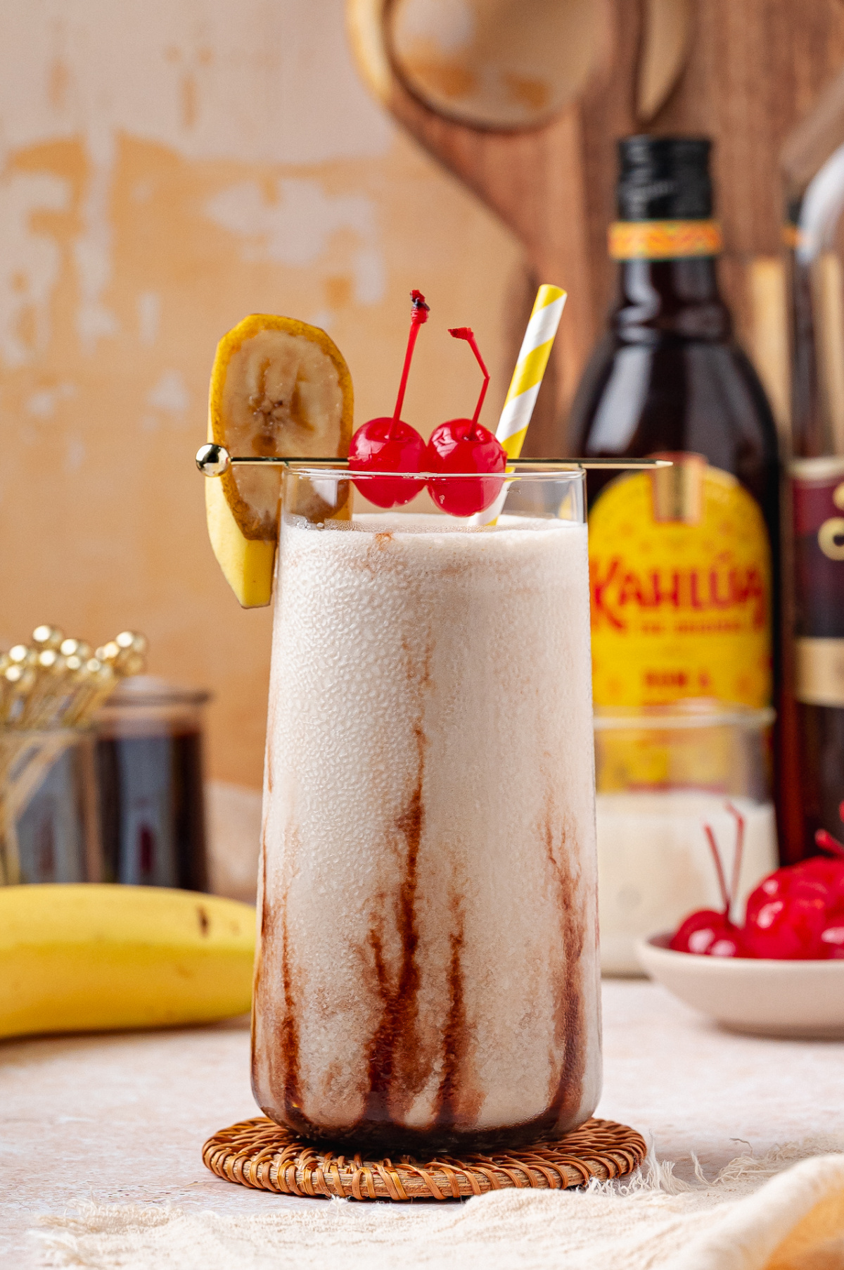 Dirty Banana cocktail in tall glass with chocolate streaks, banana slice, and maraschino cherries