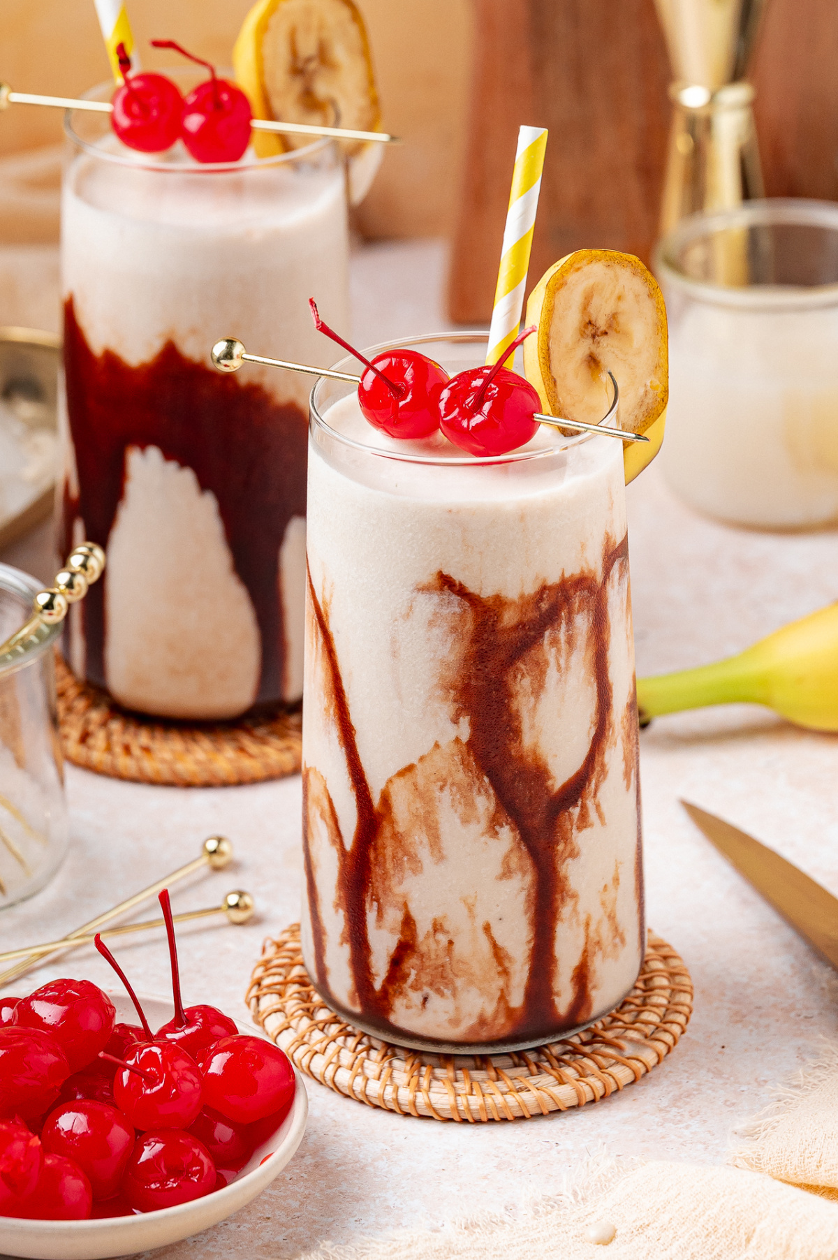 Dirty Banana cocktail with chocolate drizzle, maraschino cherries, and banana garnish in tall glass