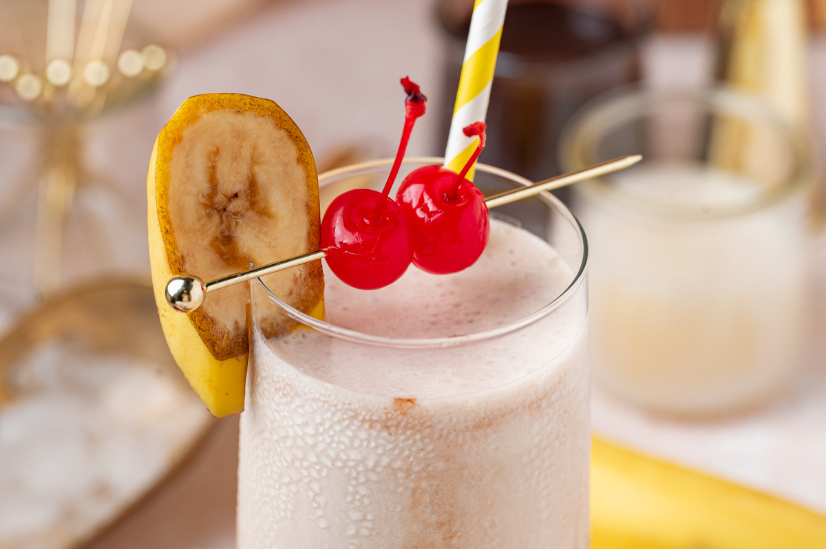 Frozen banana rum cocktail topped with maraschino cherries and fresh banana slice garnish