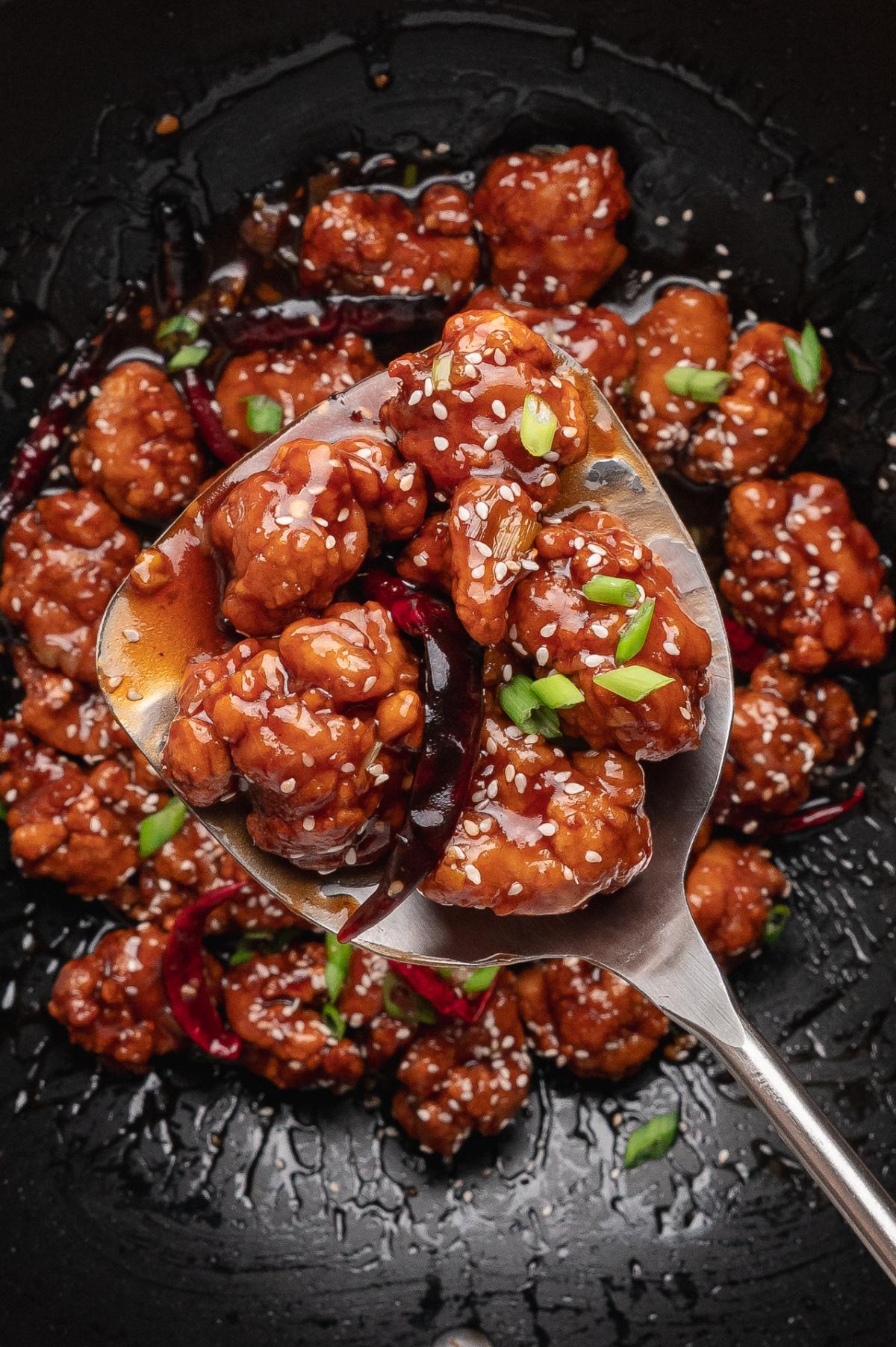 Close-up of crispy Chinese-American chicken tossed in glossy sweet and savory sauce with sesame seeds and scallions