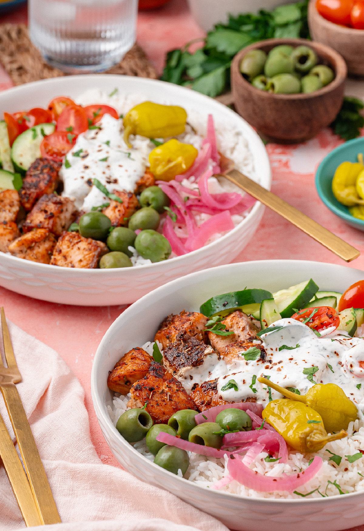 Greek Salmon Rice Bowl with seared salmon bites, white rice, olives, cherry tomatoes, cucumber, pepperoncini, and yogurt dill sauce