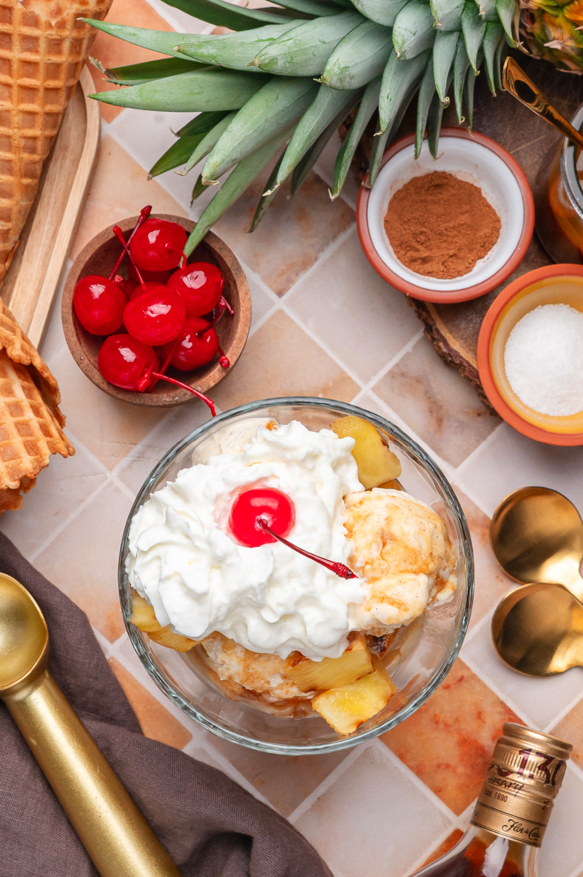Overhead view of grilled pineapple with vanilla ice cream, whipped cream, cherries, cinnamon, and rum