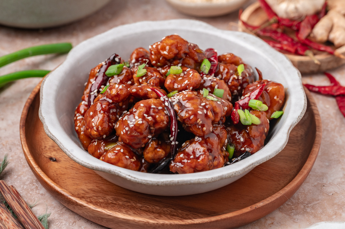 Close-up of General Tso&rsquo;s chicken in a bowl with sesame seeds, scallions, and dried red chilies