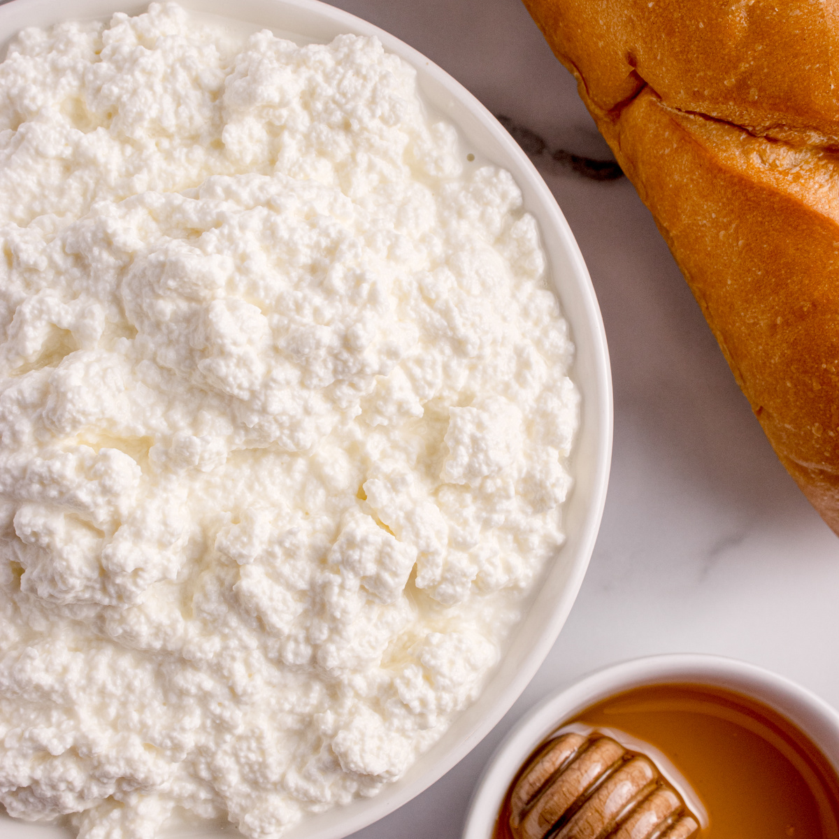 Creamy homemade ricotta cheese served in a bowl with bread and honey