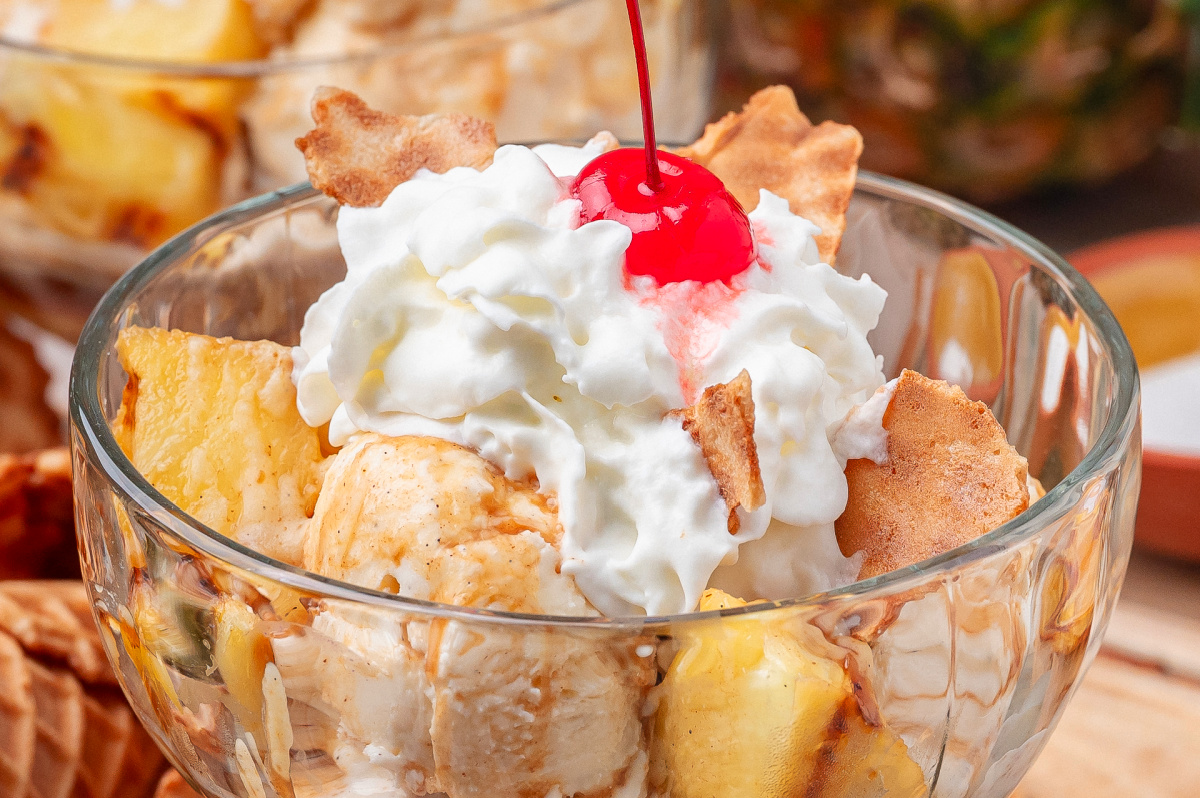 Close up of grilled pineapple with vanilla ice cream, whipped cream, and hot buttered rum sauce