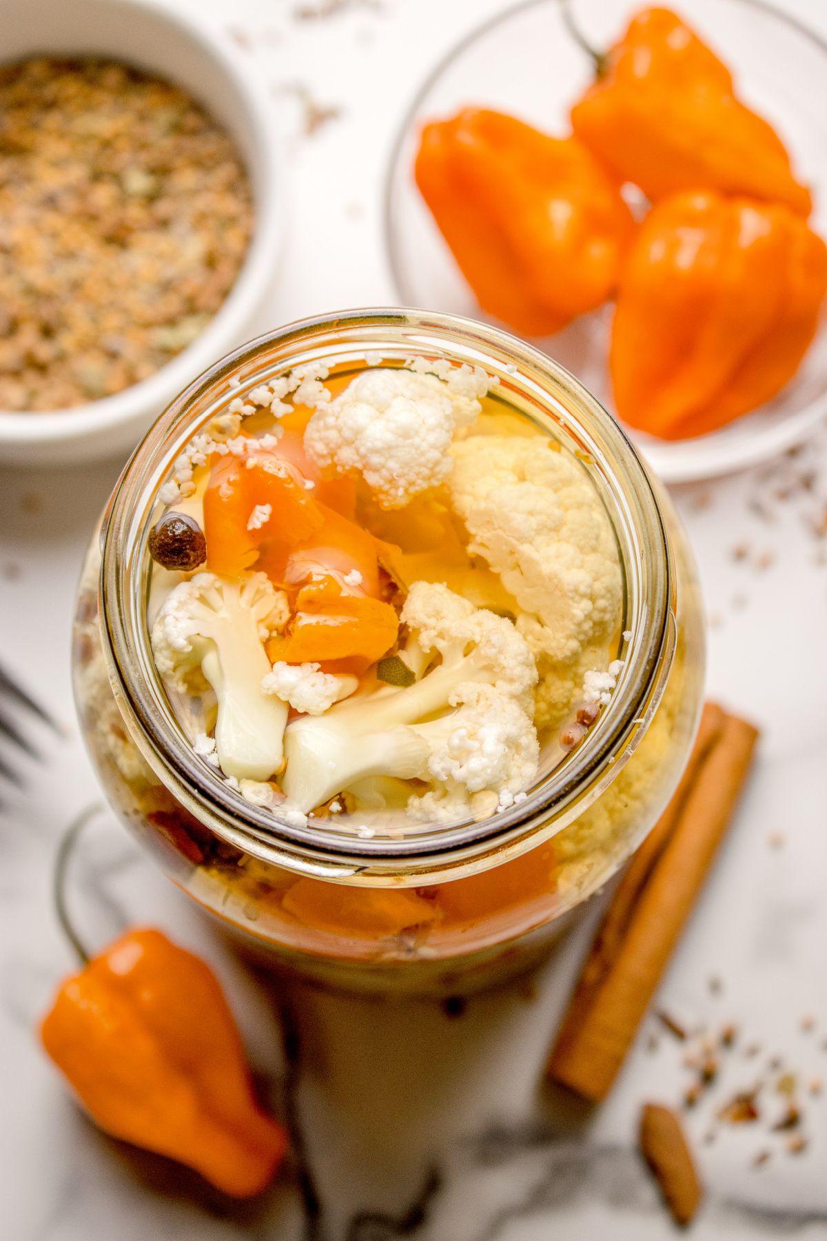 Hot pickled cauliflower in a glass jar with sliced habaneros and whole spices in vinegar brine