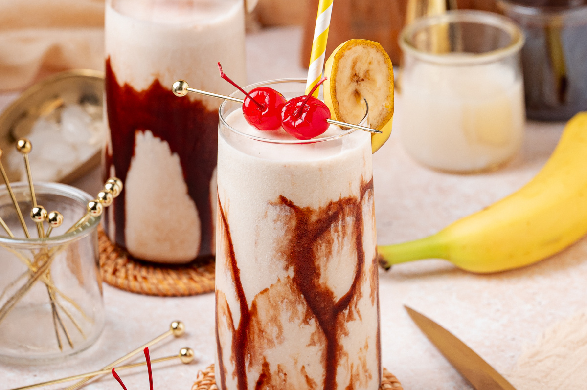 Dirty Banana cocktail with chocolate syrup swirls, banana garnish, and maraschino cherries
