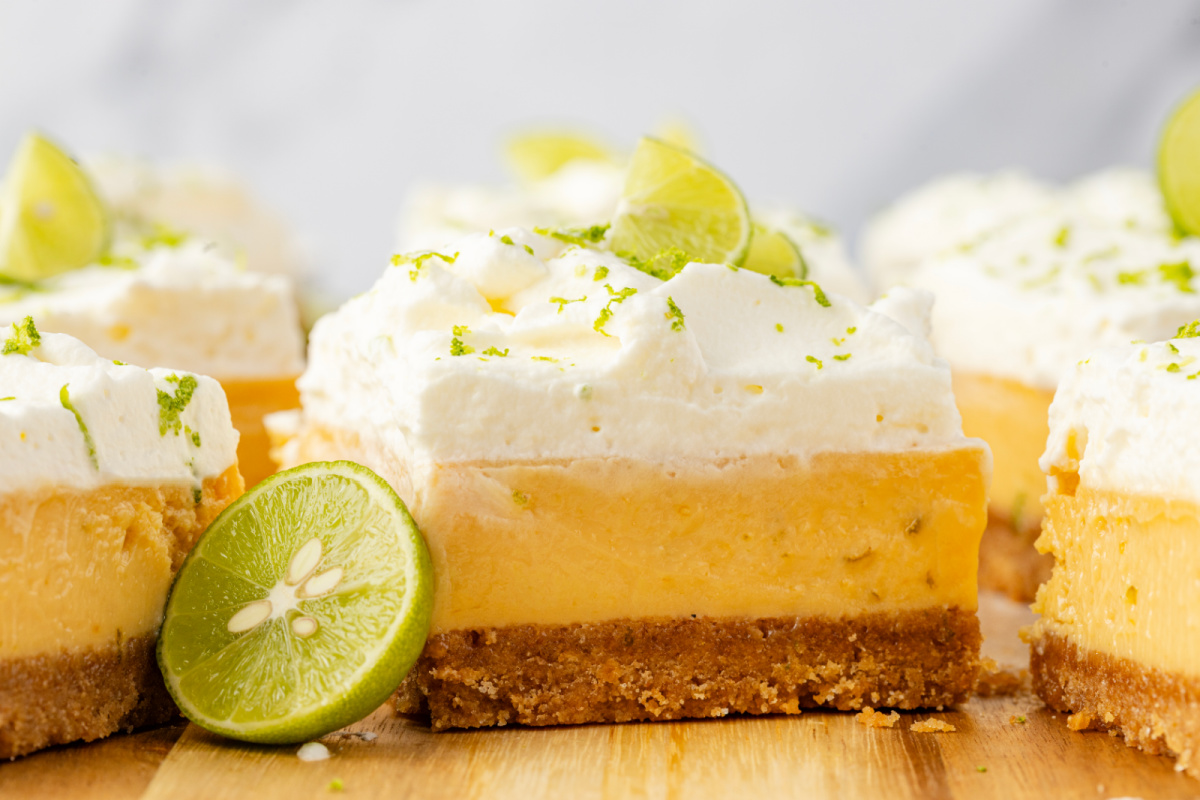 Thick lime custard bars with whipped cream topping and graham cracker crust on wooden board