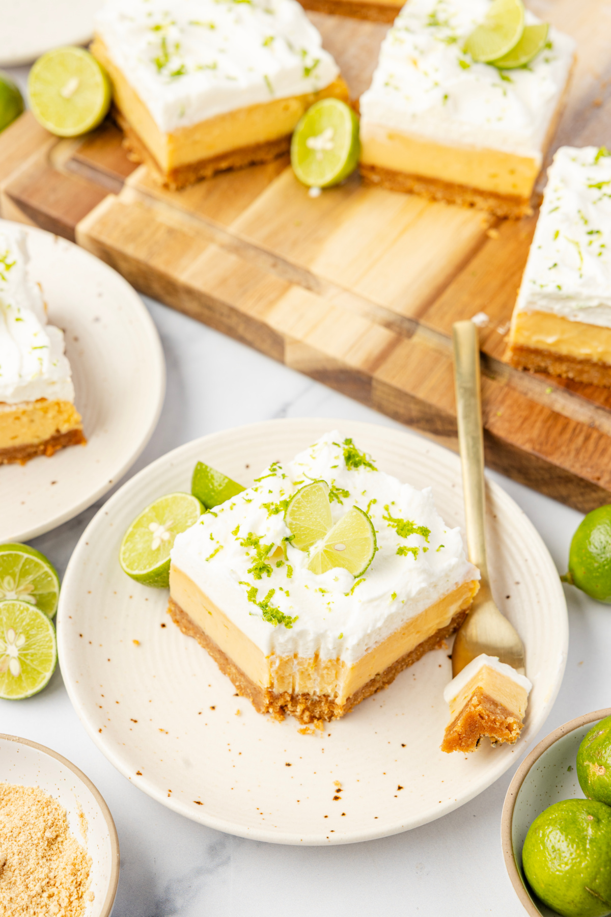 Key lime bars served on plates with whipped cream topping, fresh lime zest, and graham cracker crust