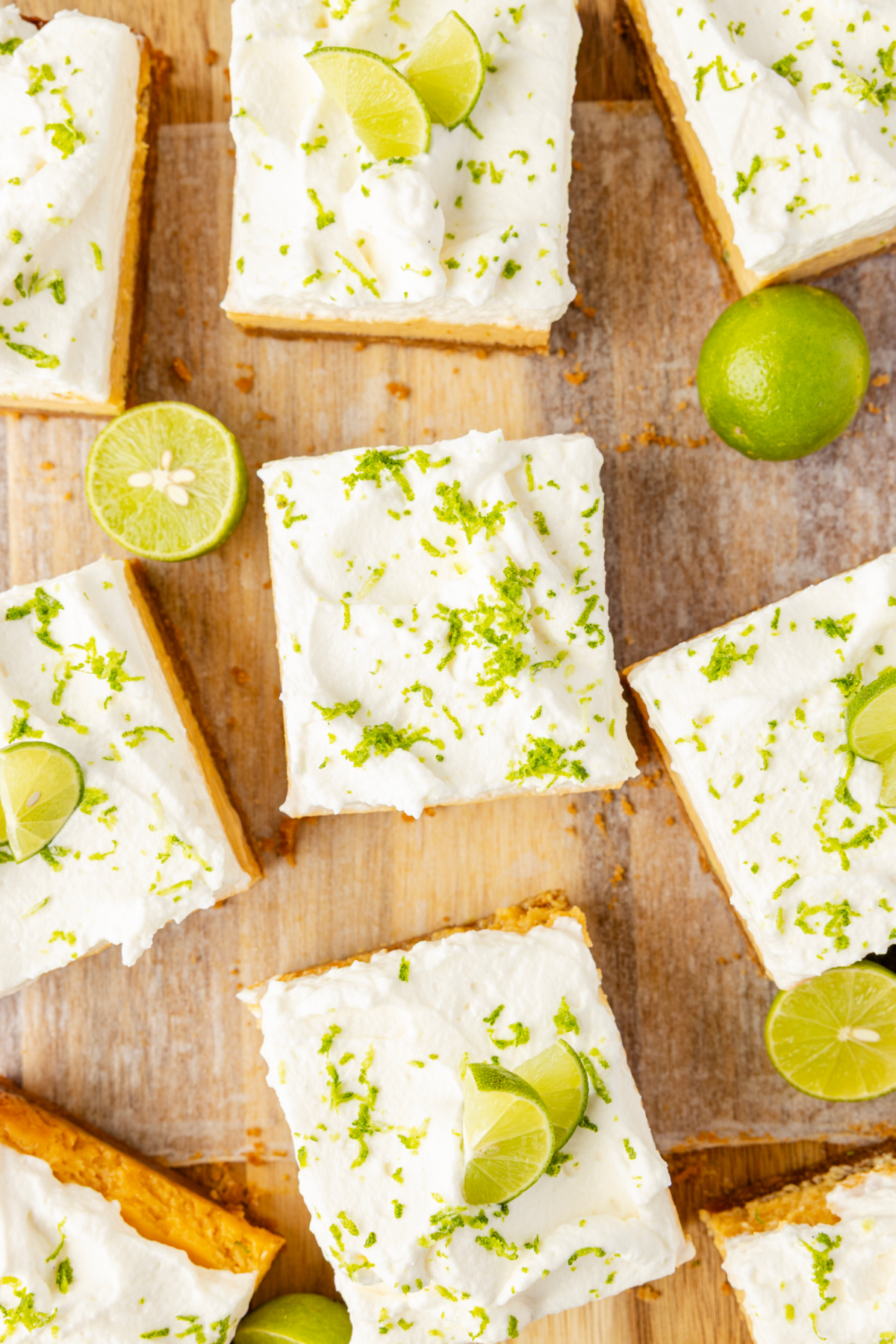 Overhead view of key lime bars topped with whipped cream and fresh lime zest on wooden board