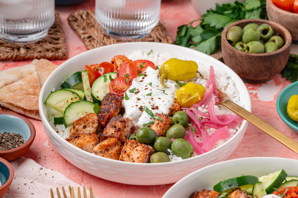 Salmon rice bowl with seared salmon cubes, white rice, cucumber, cherry tomatoes, olives, pepperoncini, and yogurt dill sauce