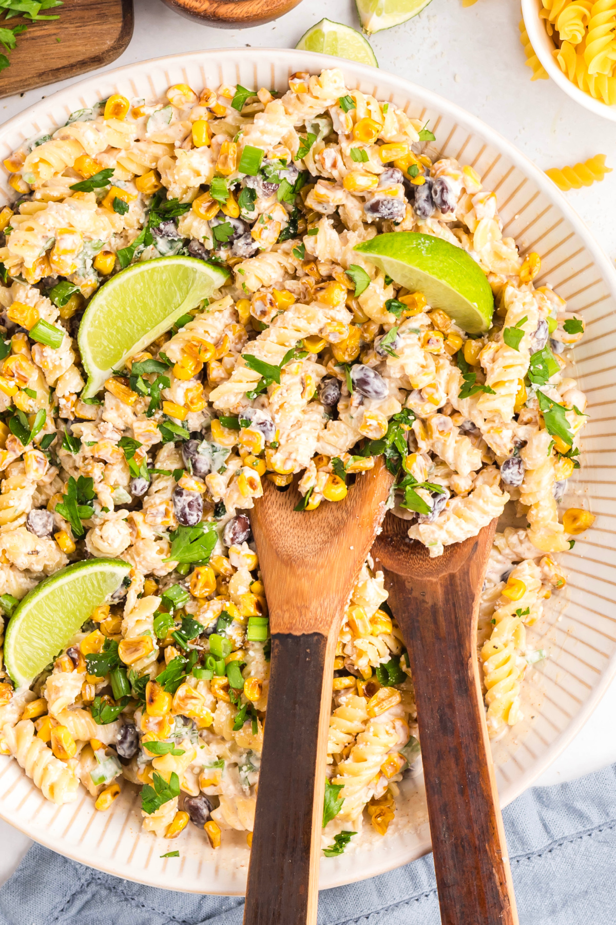 Mexican street corn pasta salad with rotini, roasted corn, black beans, cotija, and lime wedges