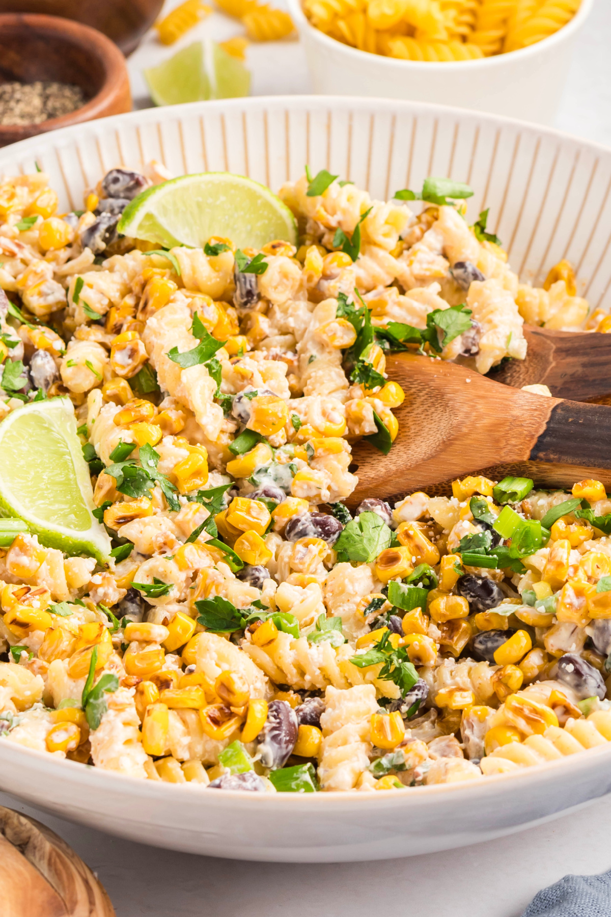 Mexican street corn pasta salad with golden saut&eacute;ed corn, cotija cheese, cilantro, and lime wedges in a serving bowl